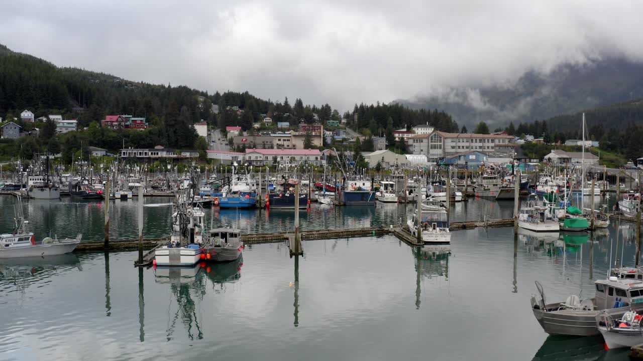 미국 알래스카의 배경에 있는 숲속 산지의 구조물과 함께 잔잔한 물에 배와 요트가 정박해 있습니다.