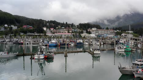 barcos y yates amarrados en aguas tranquilas con estructuras en el paisaje montañoso del bosque al fondo en alaska, ee.uu.