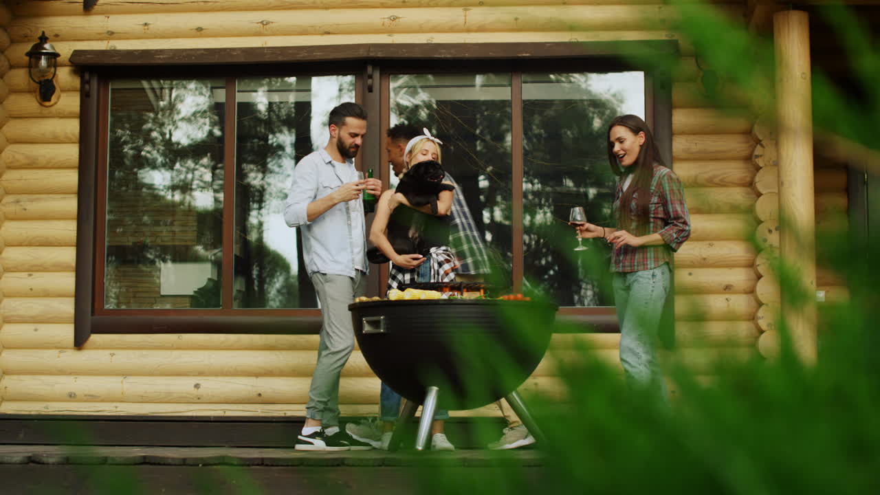 Cheerful multi ethnic friends cooking grilled meal on grate near forest house.