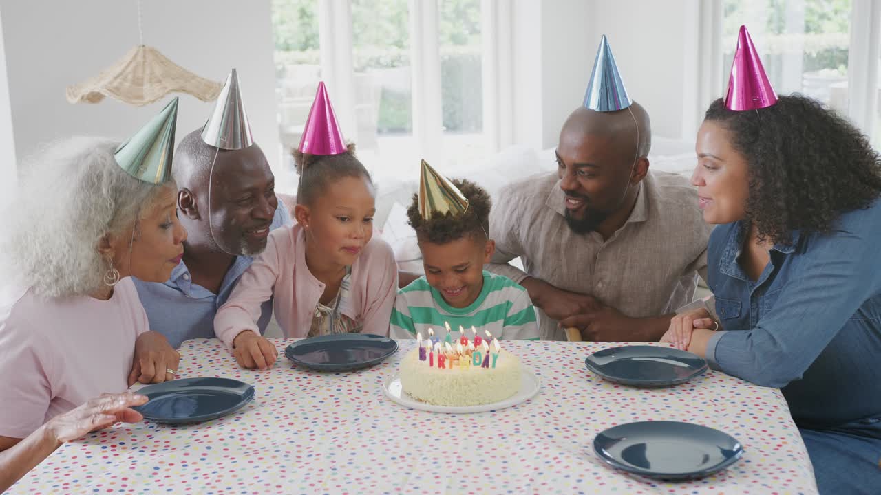 Multi Generation Family Sitting Around Table At Home Celebrating Boy's Birthday With Cake And Party