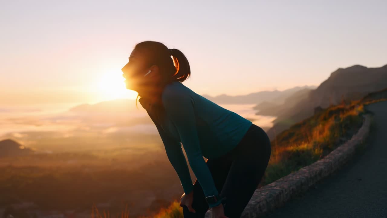 A low-angle video shot of a woman resting after a run, with a scenic sunrise backdrop