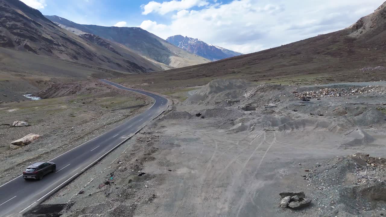Aerial drone shot following a car moving smoothly along a straight mountain stretch under clear skies.