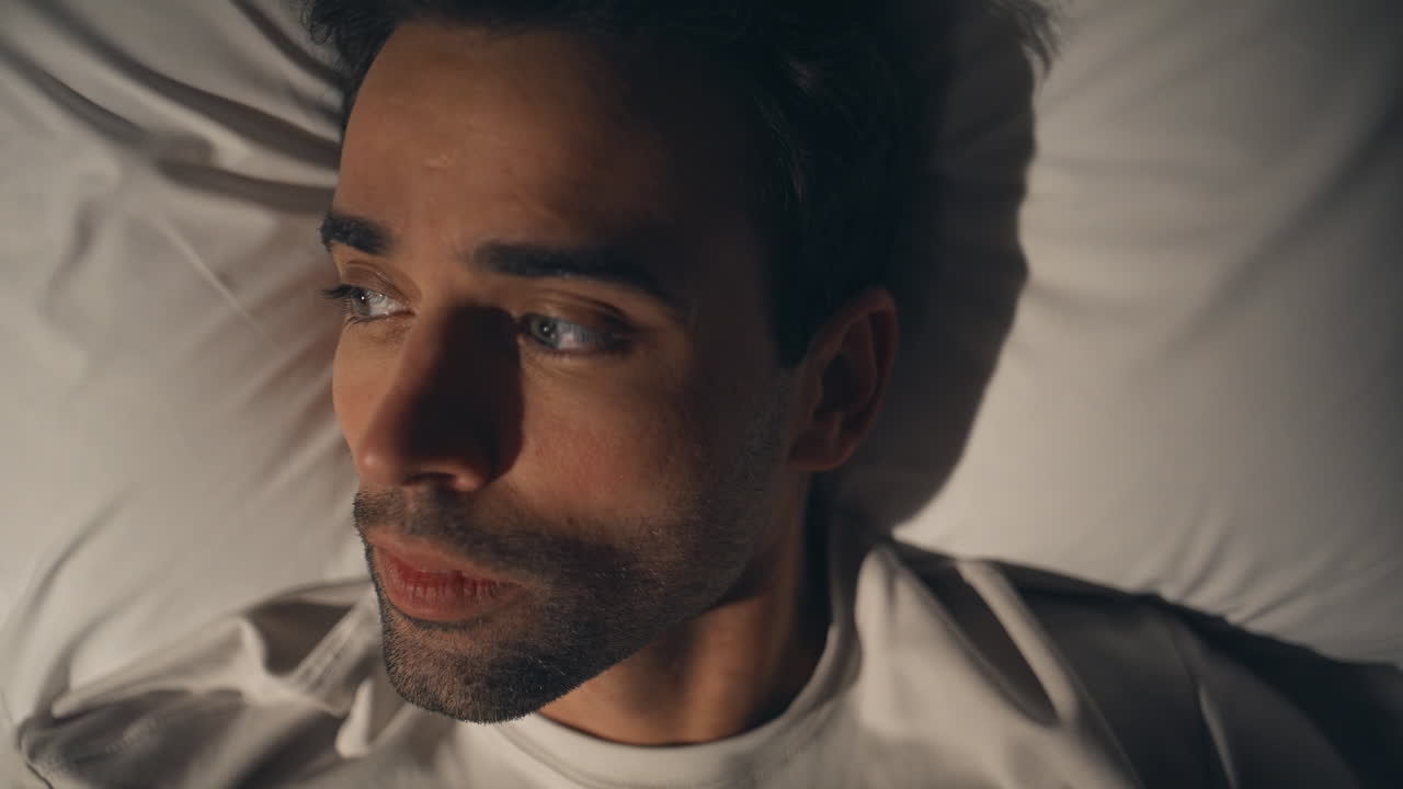 Man feeling anxiety bed dark apartment closeup. Sad guy experiencing headache