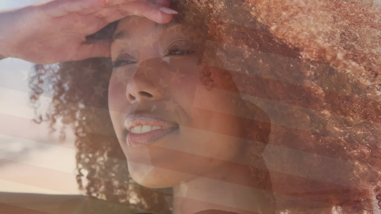 Animation of flag of united states of america over happy african american woman on beach