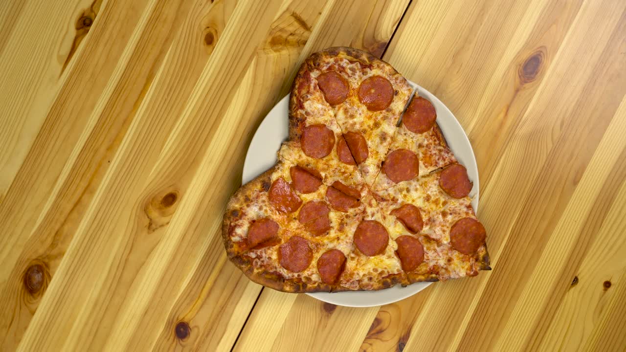 pizza en forma de corazón para el día de san valentín. la cámara gira y se acerca a la pizza. vista desde arriba.