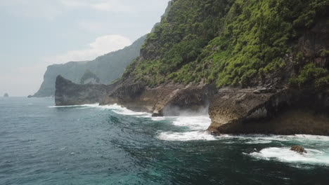 ocean waves break against base of steep tropical jungle cliffs in bali