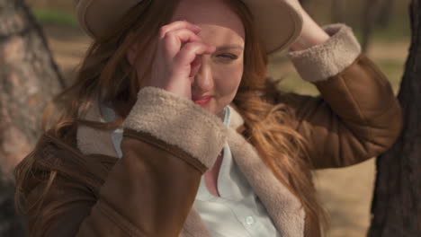 portrait of a beautiful smily red haired female wearing a camel hat in the forest