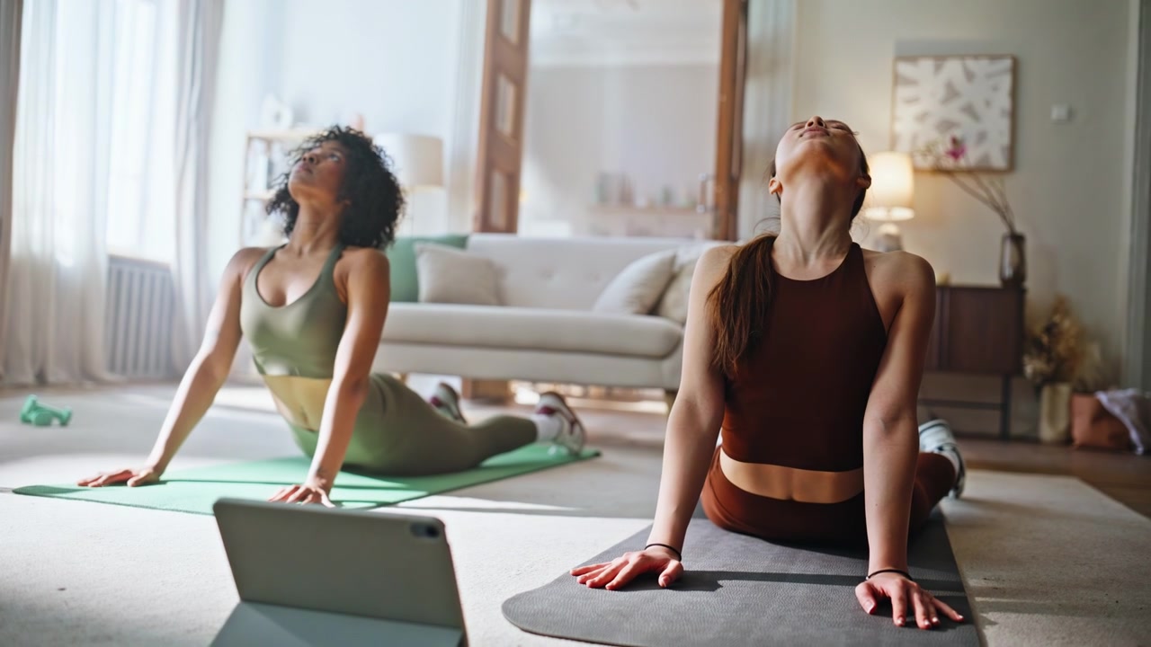 Due donne che fanno yoga a casa seguendo un tutorial online su tablet. Allenamento posa del cobra