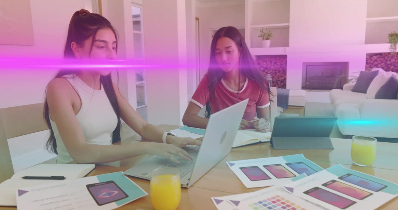 Diseñadores encendiendo el portátil y hojeando notas en la mesa del comedor, animando maquetas de UI para una revisión de diseño.
