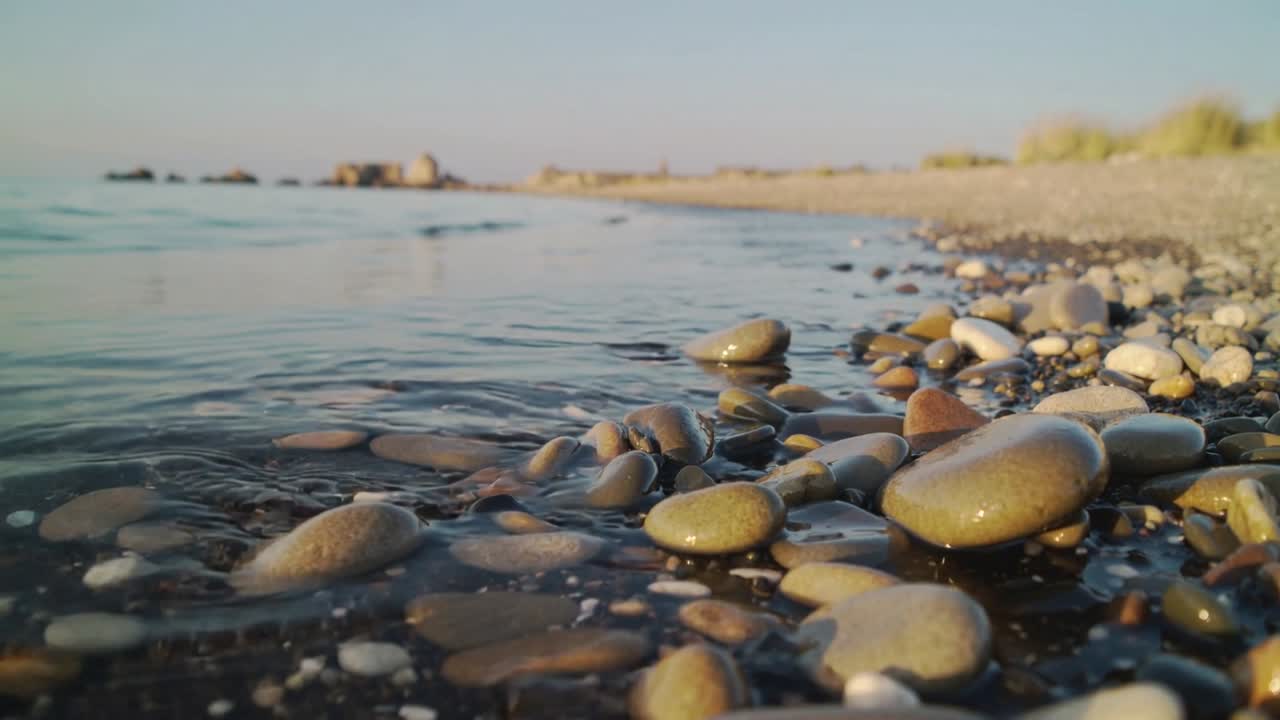 A ondulação que avança pela costa de seixos, molhando as pedras lisas e formando espuma.