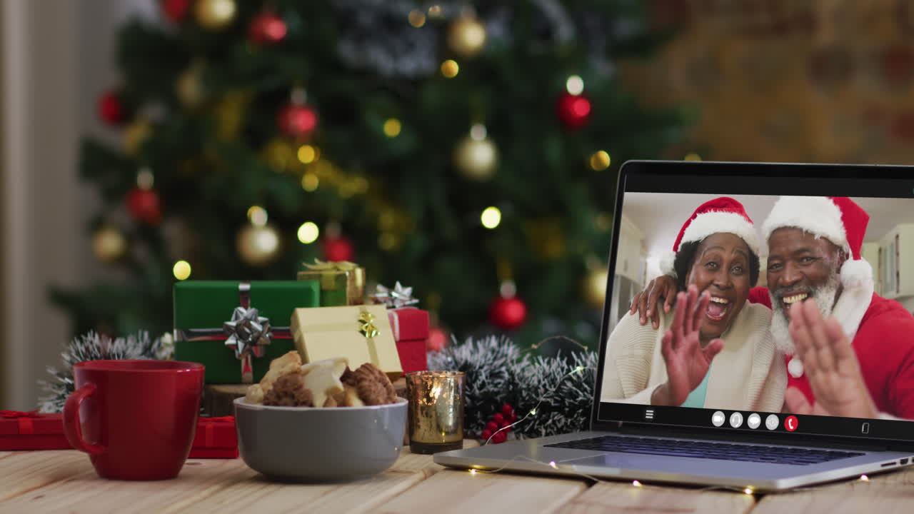 una pareja de ancianos afroamericanos con sombreros de santa en una videollamada en una computadora portátil, con un árbol de navidad