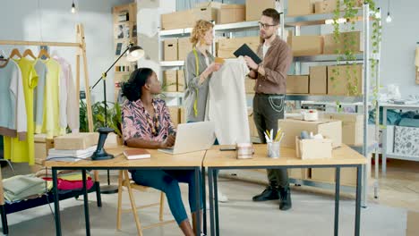 Caucasian-male-manager-typing-on-tablet-and-talking-to-female-designer-in-clothing-shop-while-African-american-coworker-typing-on-laptop