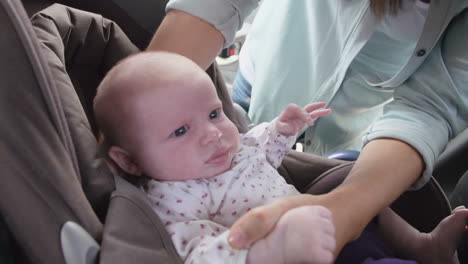 mother putting baby daughter in safety seat on car journey