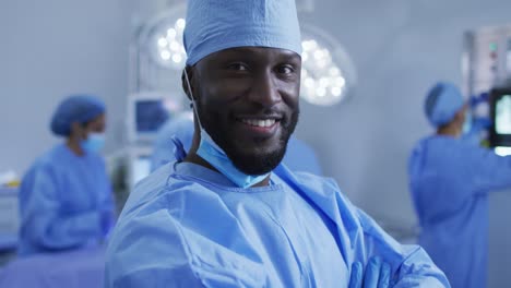portrait of african american male surgeon standing in operating theatre smiling to camera