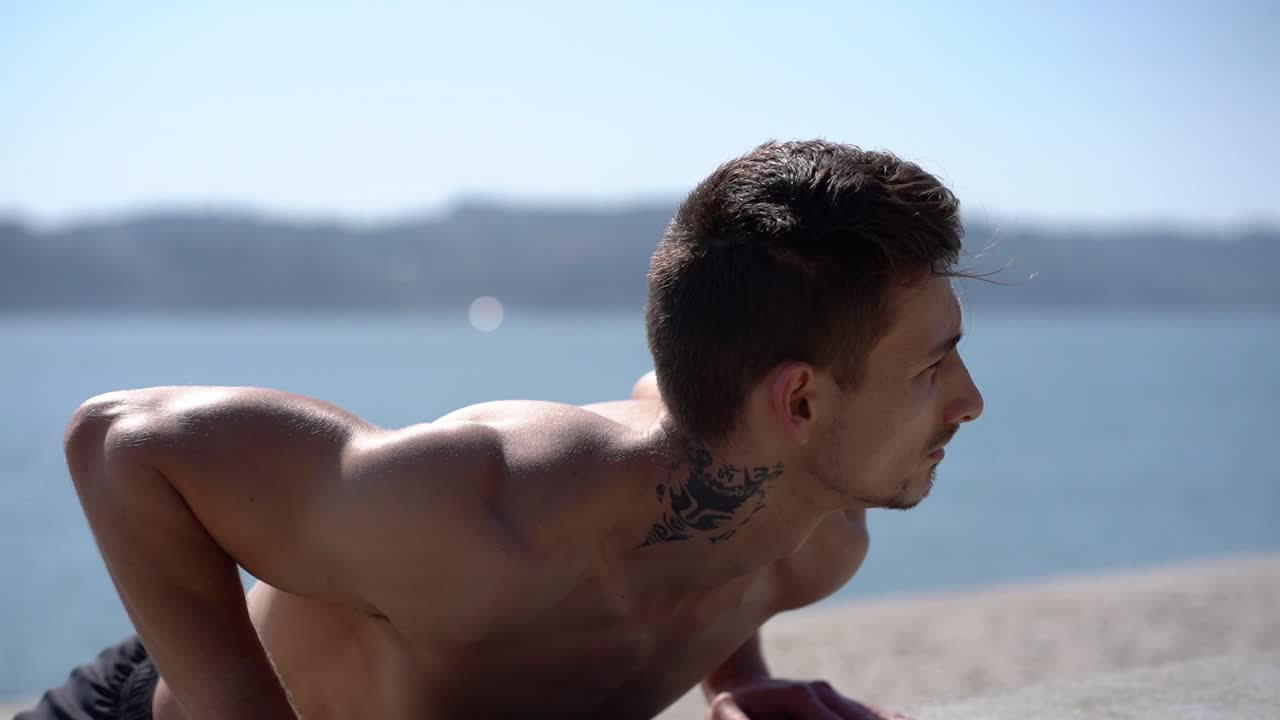 concentrado atleta tatuado haciendo flexiones en la orilla del río