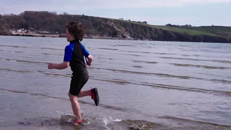 young boy runs enthusiastically on beach through the surf on a bright day