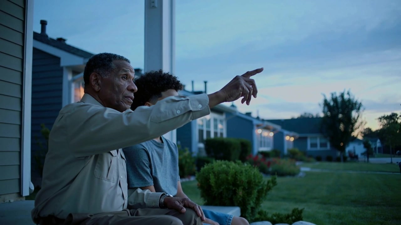 Spotting bright object older man pointing toward dusk sky on porch steps, boy watching