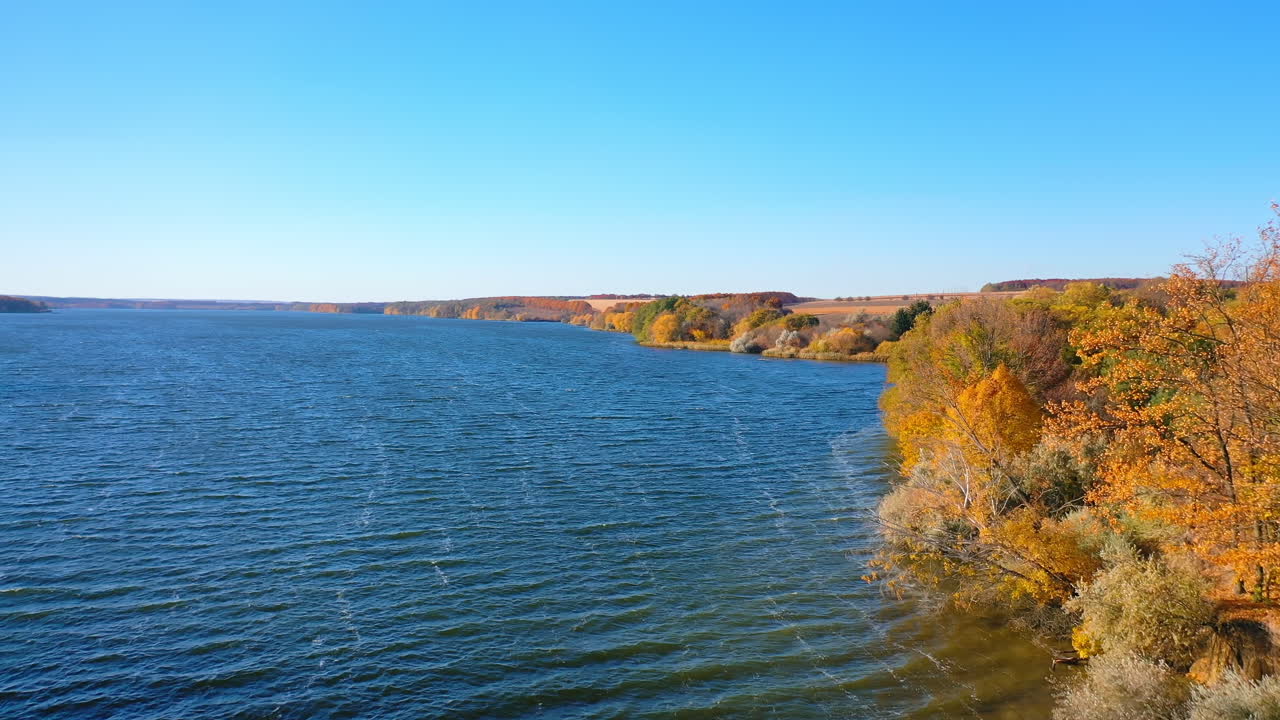 Stunning scenery of the dark blue river and colorful bank. Ripple surface of dark waters. A top view wide river and autumn forest.