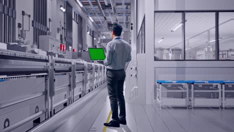 full body back view of an asian male professional worker standing at pharmaceutical factory, vaccine production facility, typing on laptop's keyboard with green screen and look at the factory once