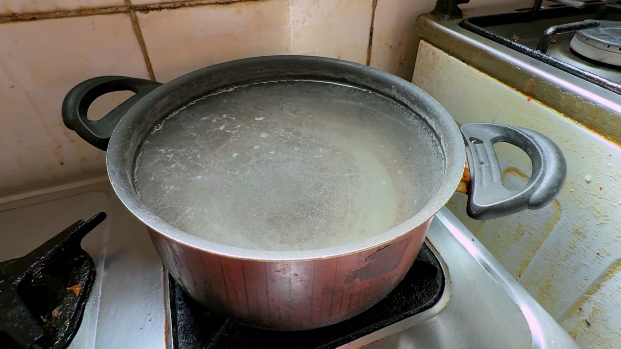 boiling water inside a metal cooking pot on a gas stove in a home kitchen, with steam, hot surface, and active burner showing everyday indoor cooking.