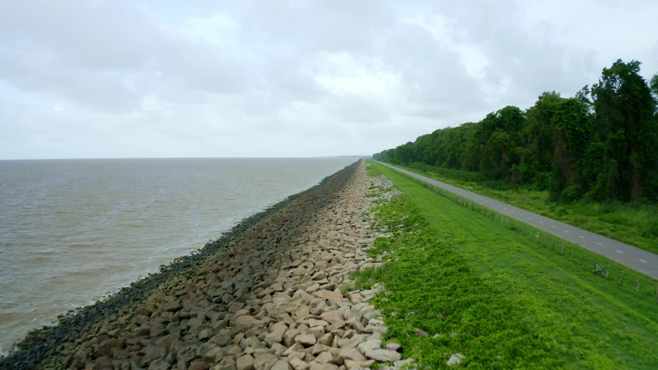 с воздуха: вид на морскую дамбу вдоль асфальтовой дороги, беспилотник, быстро летающий назад, северный атлантический океан и никери суринам