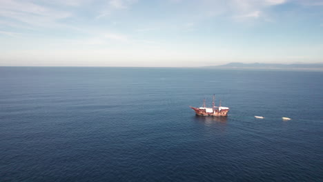 A-pirate-style-wooden-ship-is-shown-sailing-along-the-coasts-of-Puerto-Vallarta,-Jalisco-and-Bahía-de-Banderas,-Nayarit,-with-the-drone-orbiting-the-impressive-vessel,-showing-the-distant-coastline