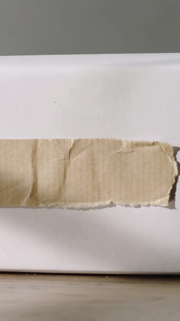 Vertical video: Pulling back shot revealing torn brown cardboard strip on white box, showing edge