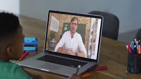 niño afroamericano haciendo la tarea mientras tiene una videollamada con un profesor masculino en una computadora portátil en casa