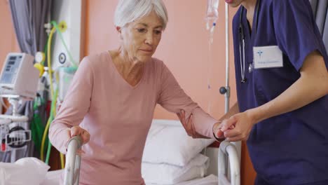 una doctora biracial ayudando a una paciente caucásica anciana a usar un marco para caminar en el hospital.