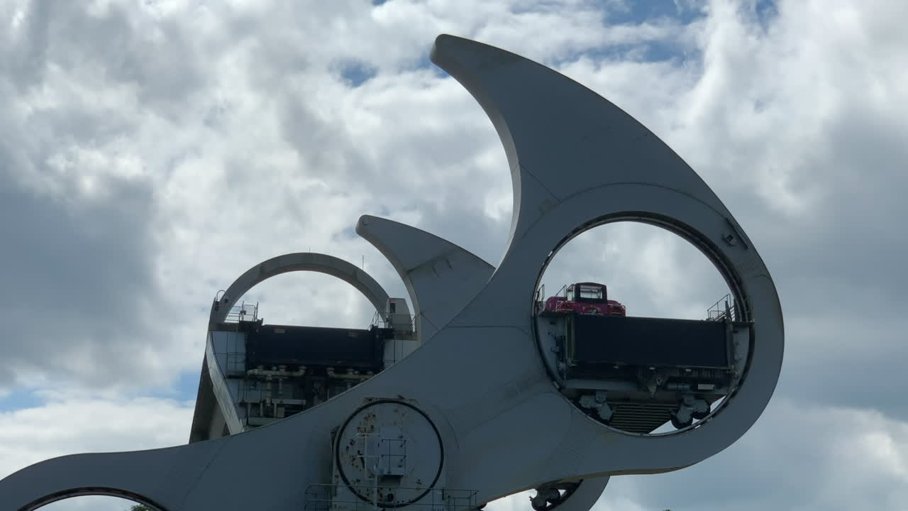 View of the Falkirk Wheel turning as it lifts a barge onto the canal above. Overcast day. Slow zoom out from the top of the Wheel.