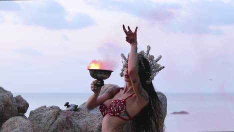beautiful, young belly dancer rotating her body and maintaining balance by holding pink color smoke bomb, on the beach. slow motion