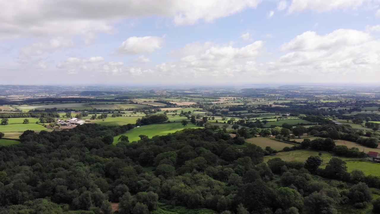 A breathtaking aerial view of the Blackdown Hills countryside showcasing lush greenery, dense forests, and picturesque open fields under a partly cloudy sky.