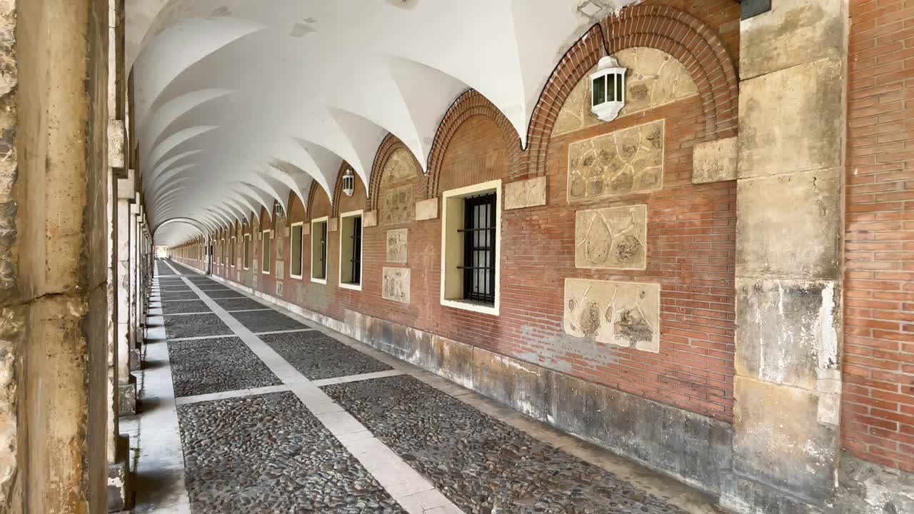 vemos uno de los pasillos exteriores de la casa comercial de aranjuez donde la vista no llega al final con sus blancos techos abovedados, sus columnas y el suelo de grava y líneas rectas.