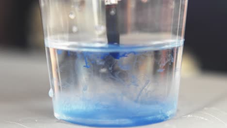 gota de pintura azul gotea y se difunde a los zarcillos en un vaso de agua, limpieza pincel de acuarela