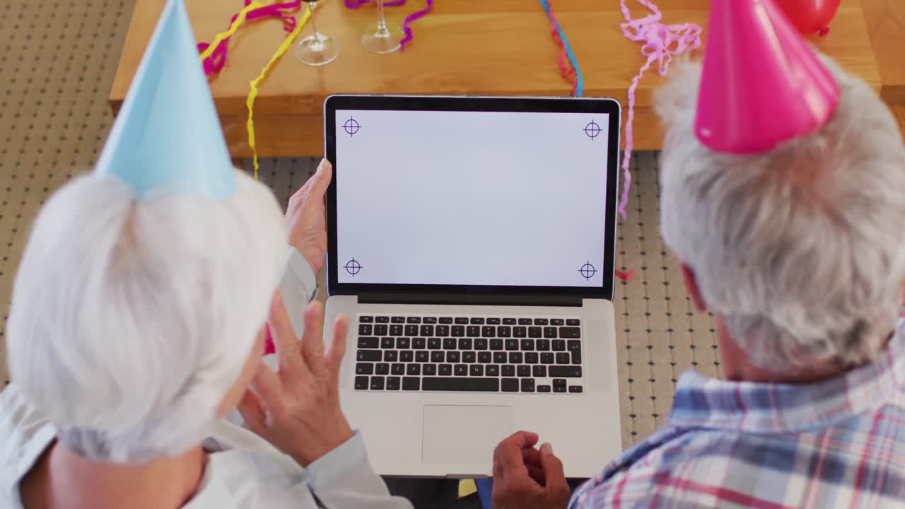 vista trasera de una pareja caucásica de alto nivel celebrando su cumpleaños mientras tienen una videollamada en una computadora portátil en casa