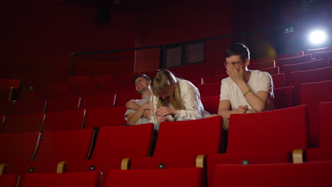 friends, a girl, and two boys enjoy a comedy movie in the cinema, low angle shot