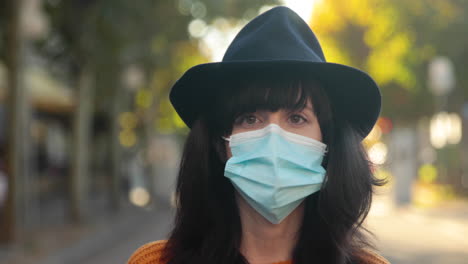 closeup of young brunette woman looking at the camera, wearing a mask and a hat