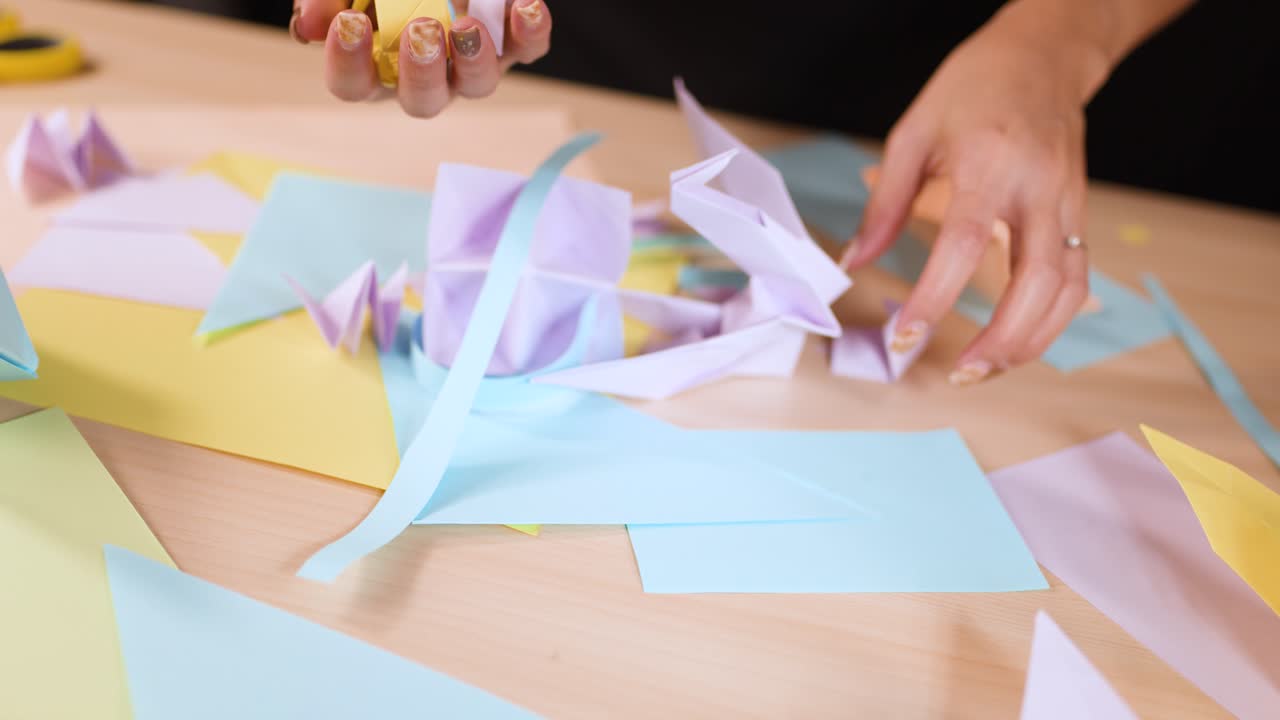 Close-up shot of hands meticulously folding and arranging pastel-colored origami paper on a wooden table