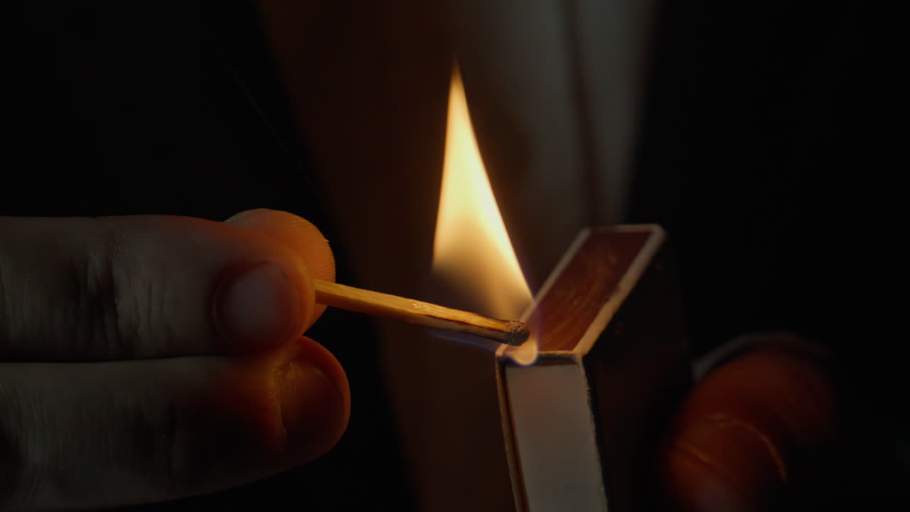 Unknown person striking match on side of box dark isolated closeup. Fire appear