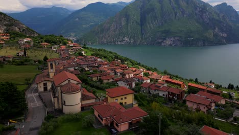 Aerial view of hillside houses with red roofs scattered across a green valley near Lake Iseo, under moody mountain skies. Shot at Riva di Solto, Lombardy, Italy (Bergamo, Lombardia)