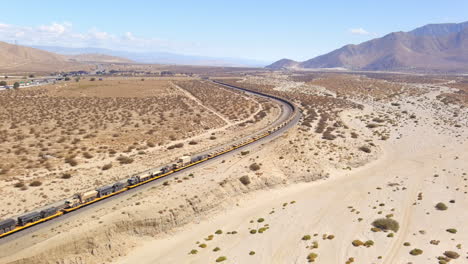 aumento de la vista aérea amplia del tren del ejército estadounidense que mueve vehículos de combate a través del desierto en california