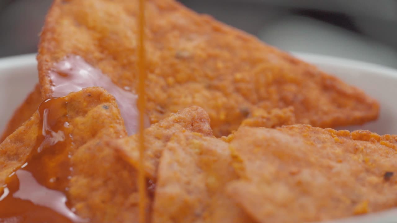 Pouring hot sauce on a bowl of crispy seasoned crackers; close-up