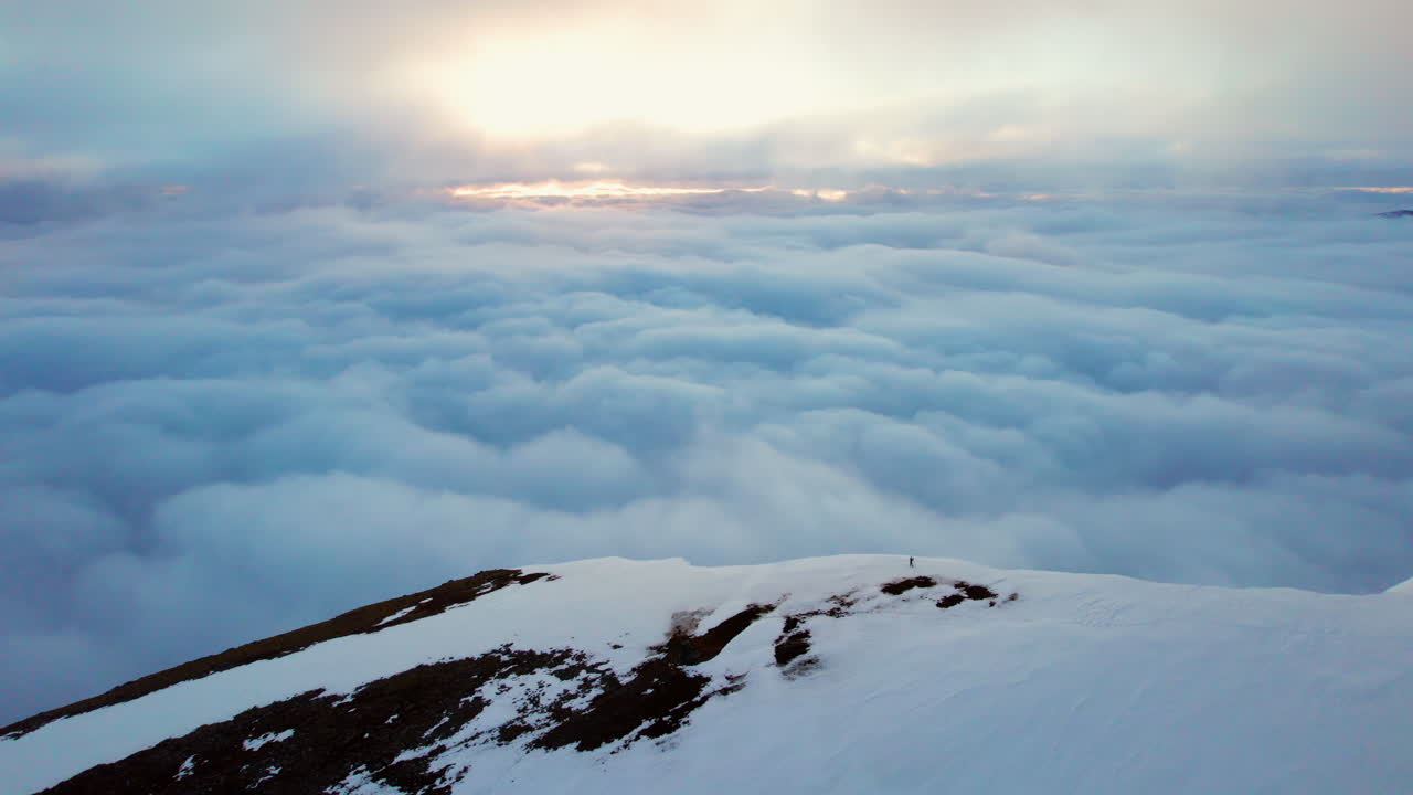 órbita aérea de un montañero en la cima con una vista increíble sobre las nubes del sol en el horizonte, sol de medianoche noruega