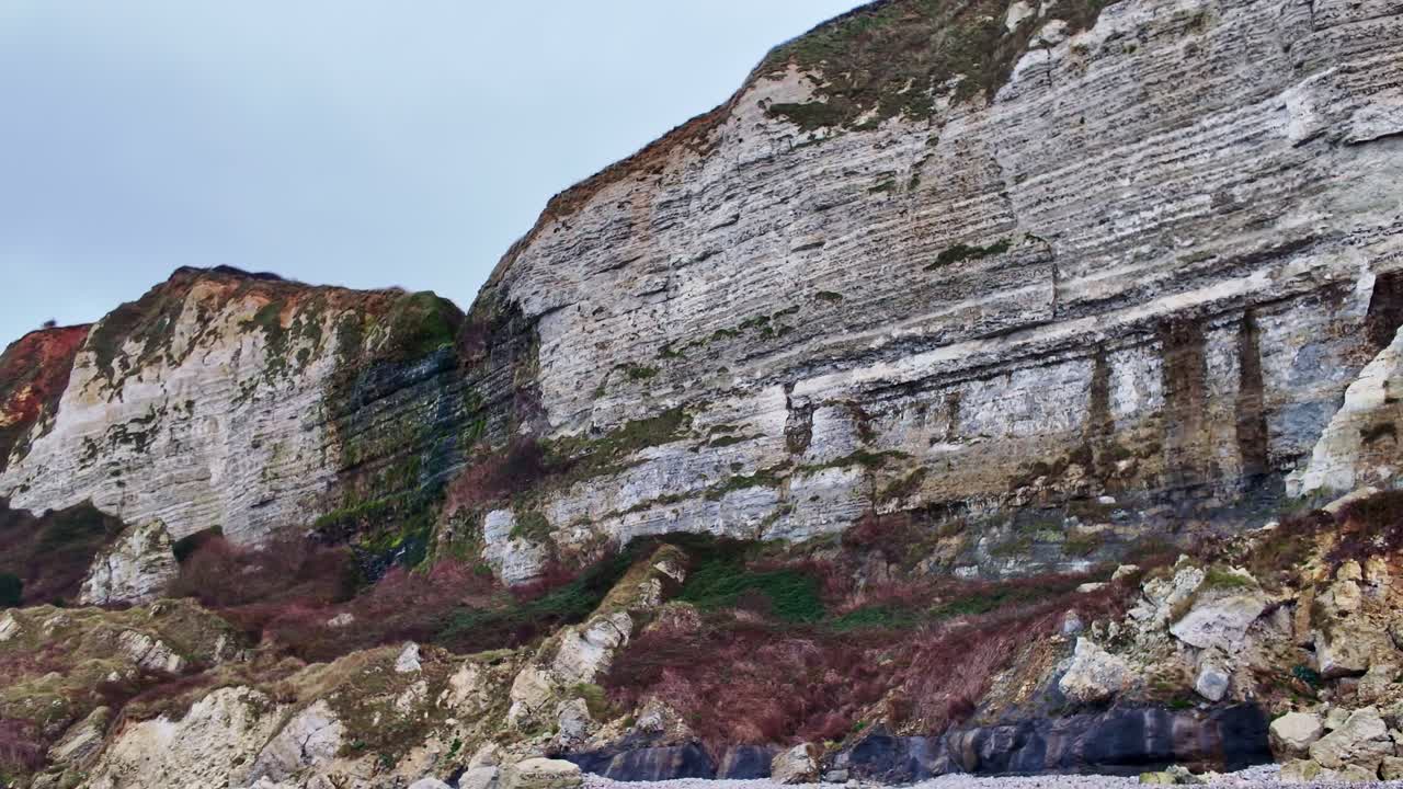 Drone panning along cliff then tilting down to rocky beach below, Saint Jouin Bruneval Beach, France