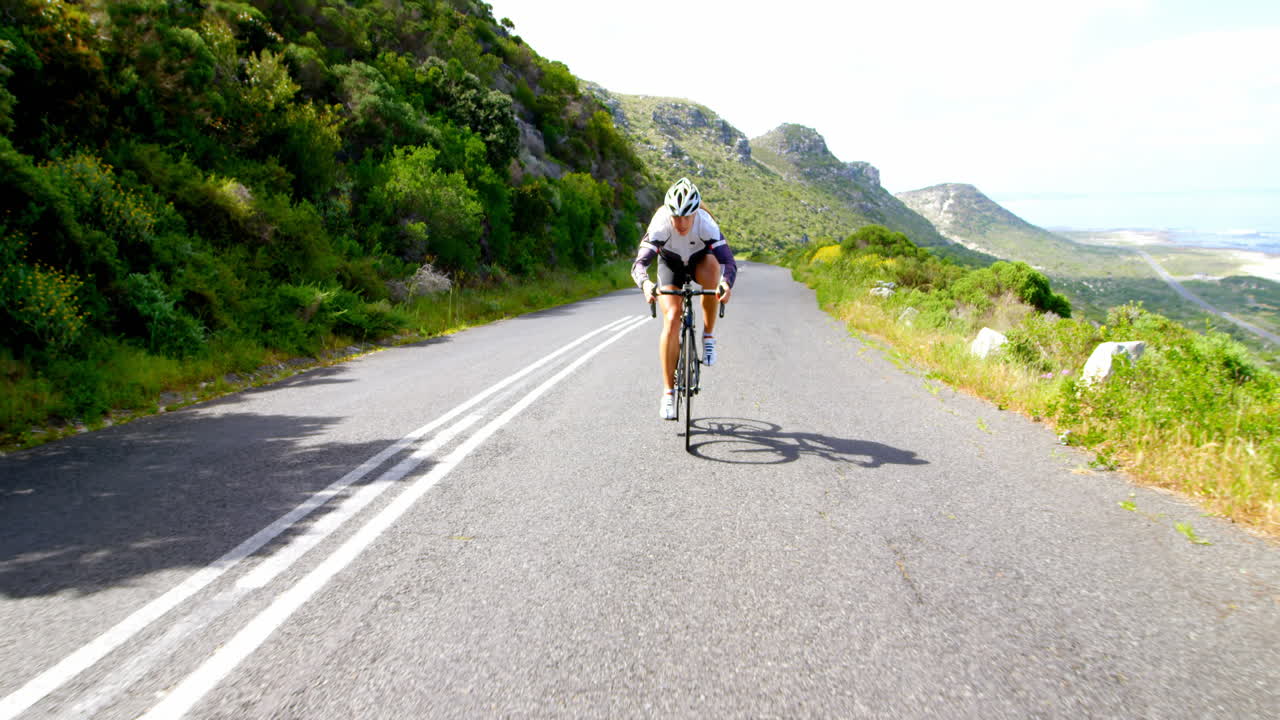 Ciclista donna in bicicletta su una strada di campagna accanto a una montagna lussureggiante, 4K.