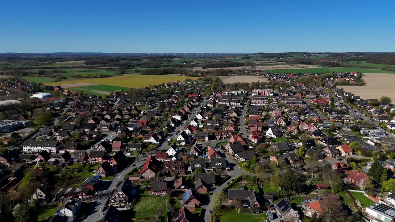 Main street leading to agricultural farm fields. Aerial lateral wide shot. American city with houses and homes during sunny day in spring season. Blue sky and colored growing cropland in distance.