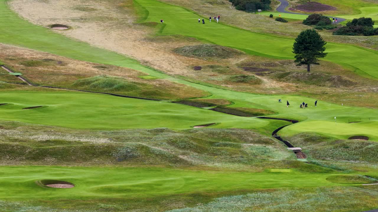 Aerial camera pans across rolling golf course fairways, greens, bunkers, and pathways in daylight