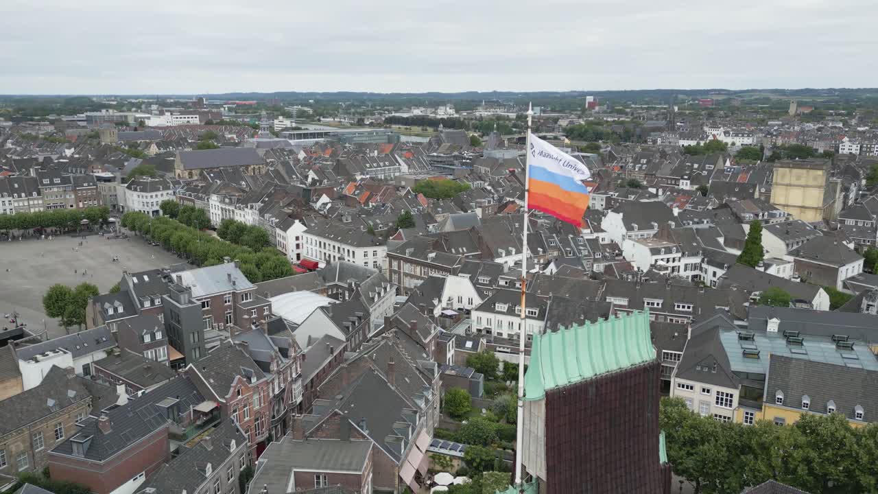 Aerial drone shot of a church tower with Dutch flag above the historic city of Maastricht, Netherlands