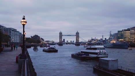 view of the tower bridge in london at dawn with boats and the bankside walkway