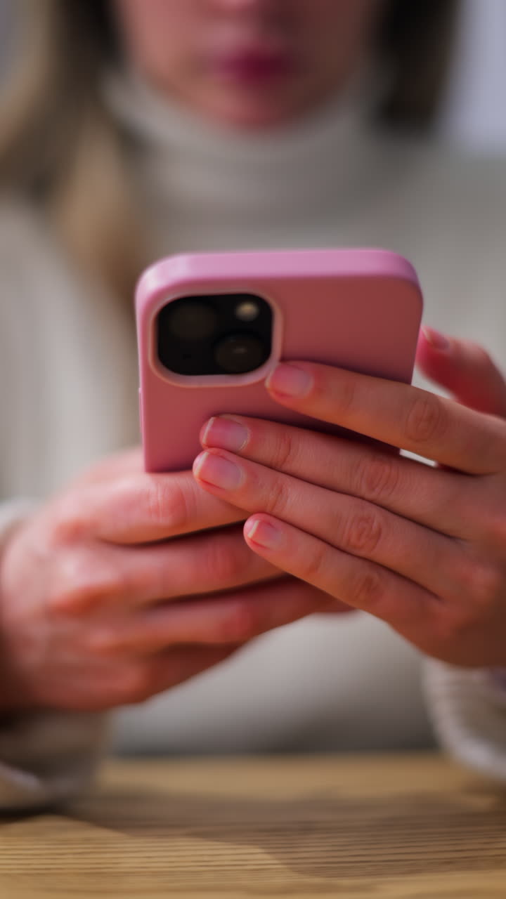 Close up of a woman in a white turtleneck scrolling on her phone. Vertical